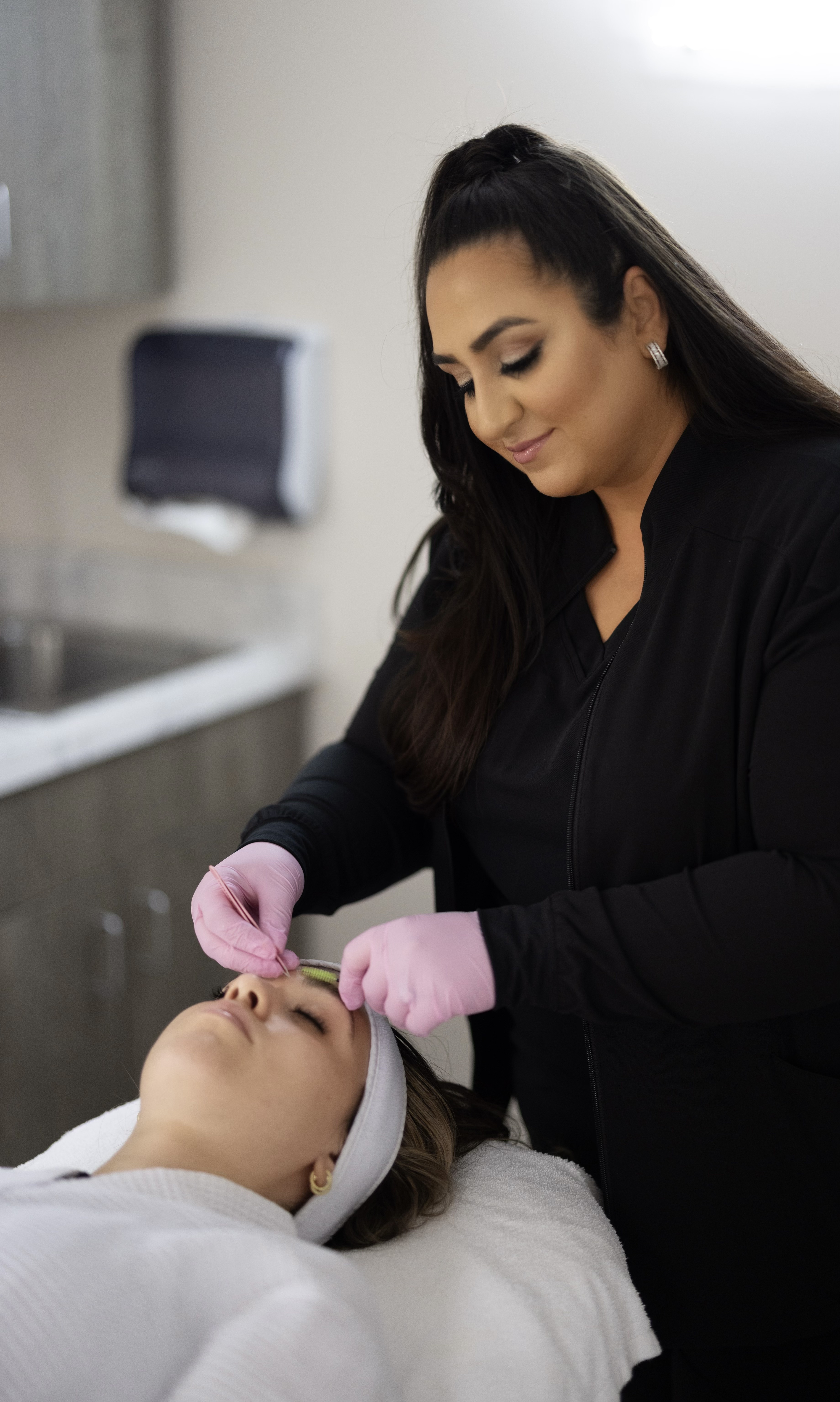 Professional nurse carefully shaping a patient's eyebrows with precision tools in a clean and serene beauty spa setting.
